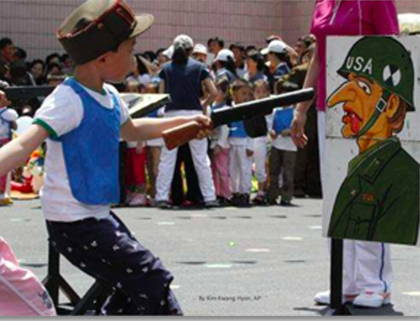 north korean toddler taking aim at a cardboard of an american soldier